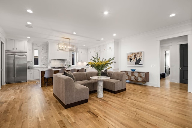 living room with crown molding, a chandelier, and light wood-type flooring