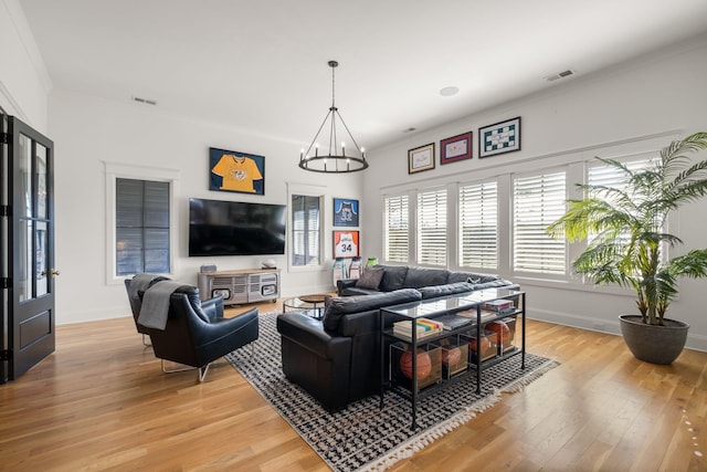 living room with crown molding, a chandelier, and light wood-type flooring