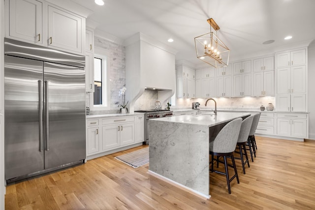 kitchen featuring decorative light fixtures, white cabinetry, a kitchen breakfast bar, high end appliances, and a center island with sink