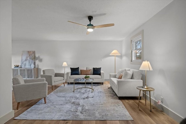 living room with ceiling fan, a textured ceiling, and light wood-type flooring