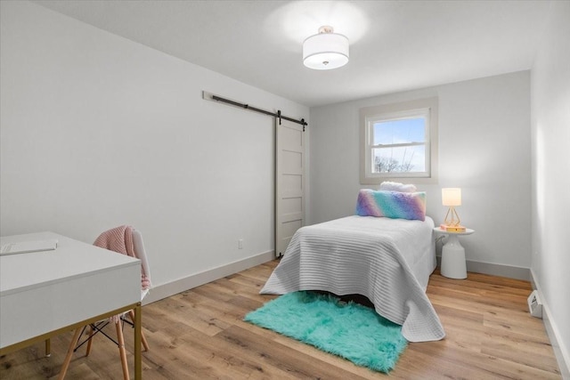 bedroom featuring a barn door, light hardwood / wood-style floors, and a baseboard heating unit