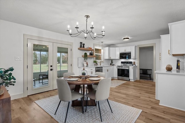 dining space with a textured ceiling, french doors, a chandelier, and light wood-type flooring