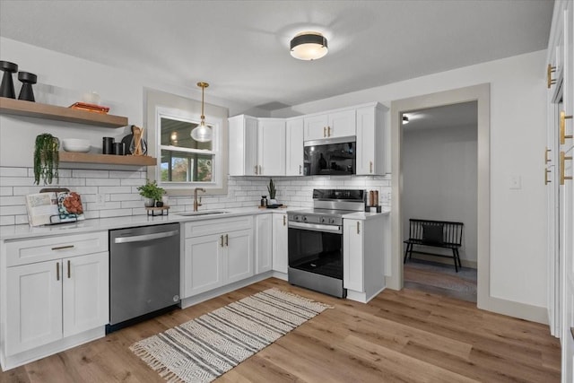 kitchen featuring sink, appliances with stainless steel finishes, white cabinetry, hanging light fixtures, and light hardwood / wood-style floors