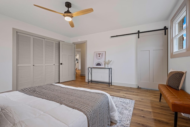 bedroom with a closet, light hardwood / wood-style floors, a barn door, and ceiling fan