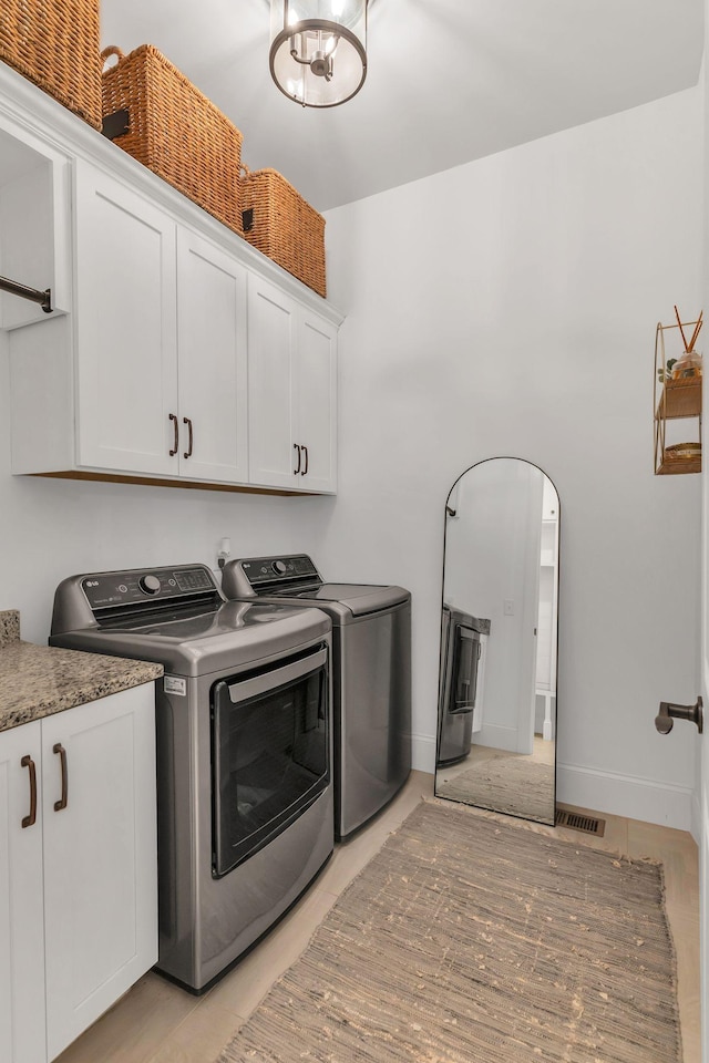 clothes washing area with cabinets and washing machine and clothes dryer