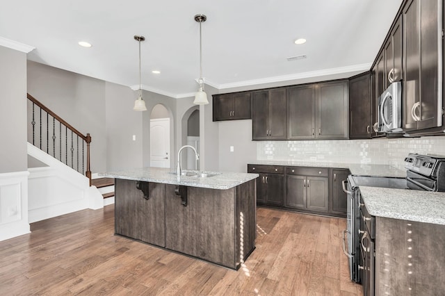 kitchen featuring sink, a center island with sink, appliances with stainless steel finishes, pendant lighting, and light stone countertops