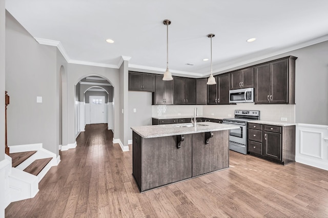 kitchen with appliances with stainless steel finishes, a breakfast bar, sink, hanging light fixtures, and a kitchen island with sink