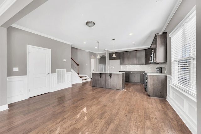 kitchen featuring dark wood-type flooring, crown molding, decorative light fixtures, a center island with sink, and stainless steel appliances