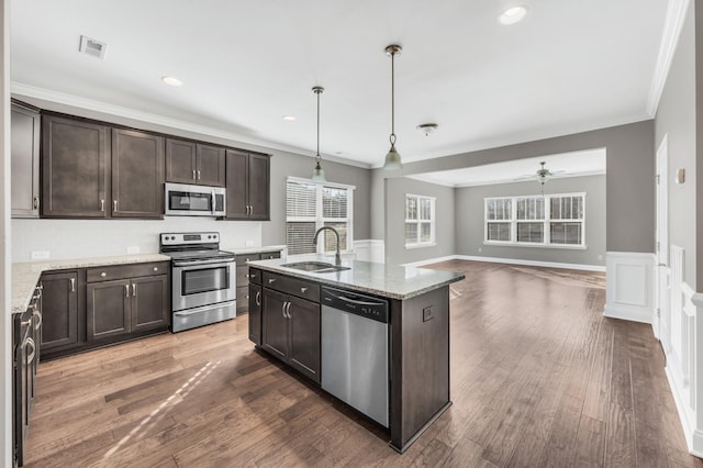 kitchen featuring appliances with stainless steel finishes, decorative light fixtures, sink, a kitchen island with sink, and light stone counters