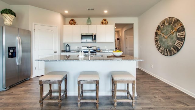 kitchen featuring stainless steel appliances, light stone countertops, a kitchen island with sink, and white cabinets