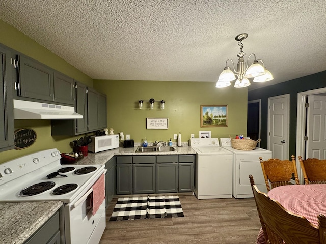 kitchen featuring washing machine and clothes dryer, sink, hanging light fixtures, white appliances, and light hardwood / wood-style floors