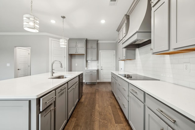 kitchen featuring sink, custom exhaust hood, decorative light fixtures, black electric cooktop, and a kitchen island with sink