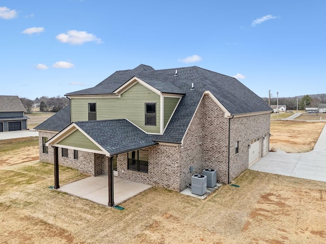 rear view of house featuring a patio, brick siding, and roof with shingles