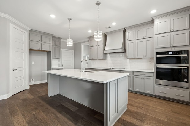 kitchen with sink, multiple ovens, black electric stovetop, decorative light fixtures, and custom exhaust hood