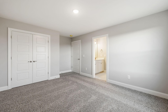 unfurnished bedroom featuring a closet, light carpet, baseboards, and ensuite bathroom