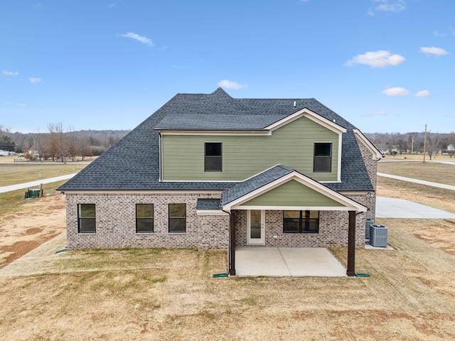 back of property with a shingled roof, a patio area, central air condition unit, a lawn, and brick siding