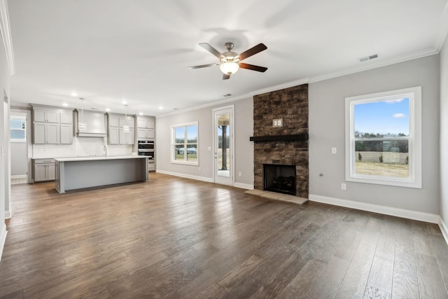 unfurnished living room with a healthy amount of sunlight, ornamental molding, and wood-type flooring