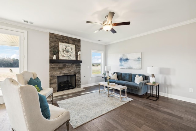 living room with visible vents, wood finished floors, a stone fireplace, crown molding, and baseboards