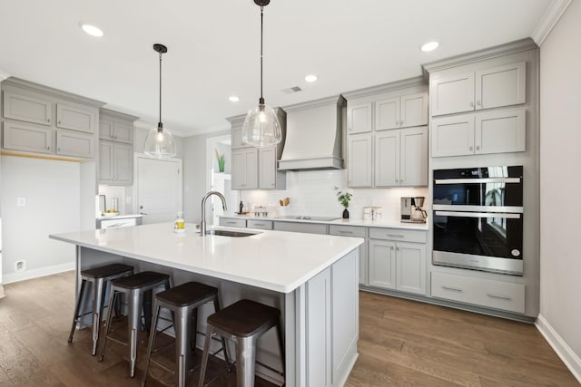 kitchen featuring dark wood finished floors, gray cabinets, a sink, custom range hood, and multiple ovens