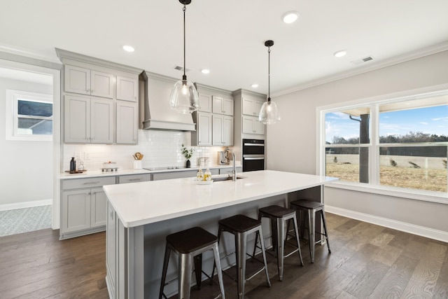 kitchen with tasteful backsplash, visible vents, premium range hood, a breakfast bar area, and a sink