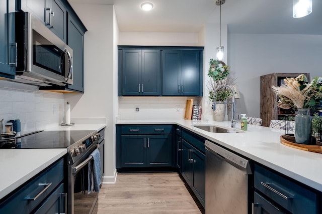 kitchen with blue cabinetry, stainless steel appliances, light hardwood / wood-style floors, and hanging light fixtures