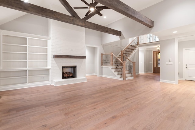 unfurnished living room with a fireplace, beamed ceiling, ceiling fan, and light wood-type flooring