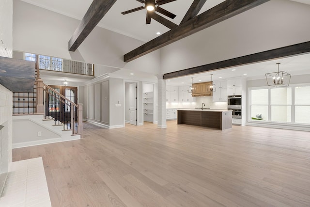 unfurnished living room featuring ceiling fan with notable chandelier, high vaulted ceiling, sink, light hardwood / wood-style floors, and beam ceiling