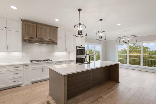 kitchen featuring pendant lighting, sink, a kitchen island with sink, white cabinets, and decorative backsplash