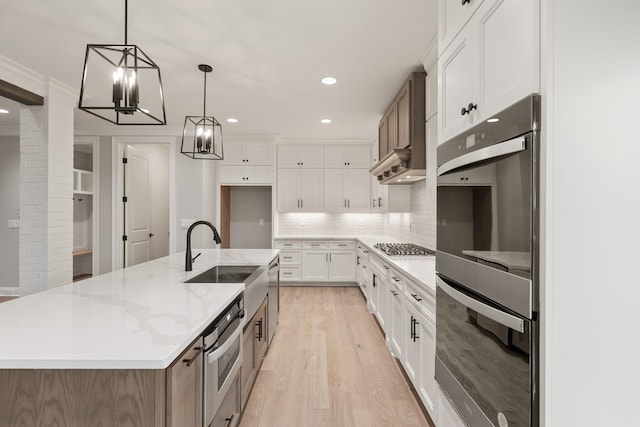 kitchen featuring pendant lighting, white cabinetry, sink, double wall oven, and a center island with sink