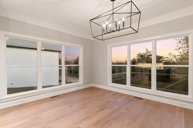 unfurnished dining area with an inviting chandelier, crown molding, and wood-type flooring