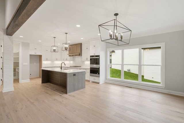 kitchen featuring sink, a kitchen island with sink, white cabinets, decorative light fixtures, and light wood-type flooring