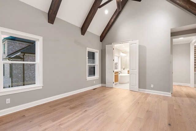 unfurnished bedroom with beamed ceiling, high vaulted ceiling, connected bathroom, and light hardwood / wood-style floors