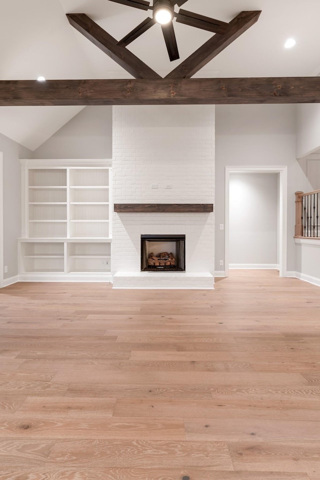 unfurnished living room with lofted ceiling with beams, ceiling fan, light hardwood / wood-style floors, and a brick fireplace