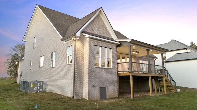 back house at dusk with a yard, central AC, a deck, and ceiling fan