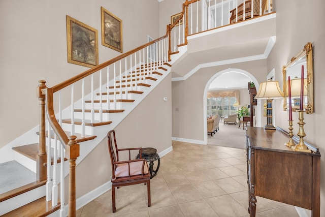 foyer with light tile patterned floors, crown molding, baseboards, arched walkways, and a high ceiling