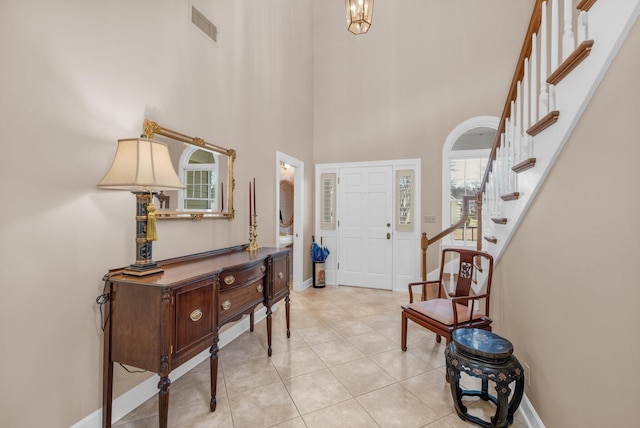 entrance foyer with stairway, visible vents, baseboards, light tile patterned flooring, and a high ceiling