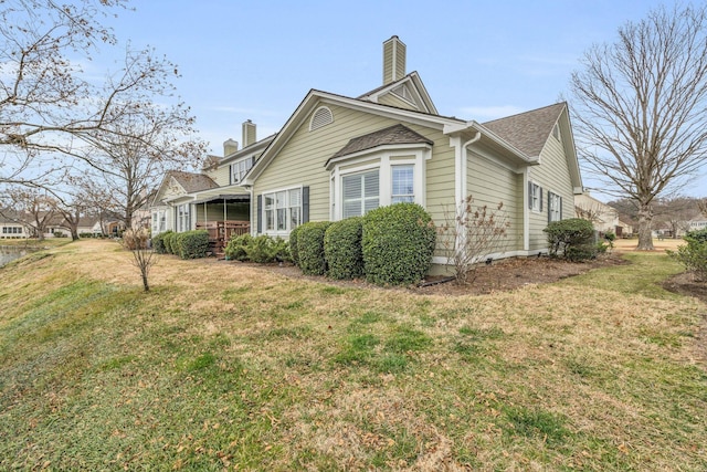 view of side of property with roof with shingles, a lawn, and a chimney