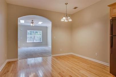 unfurnished dining area with ceiling fan with notable chandelier and light wood-type flooring