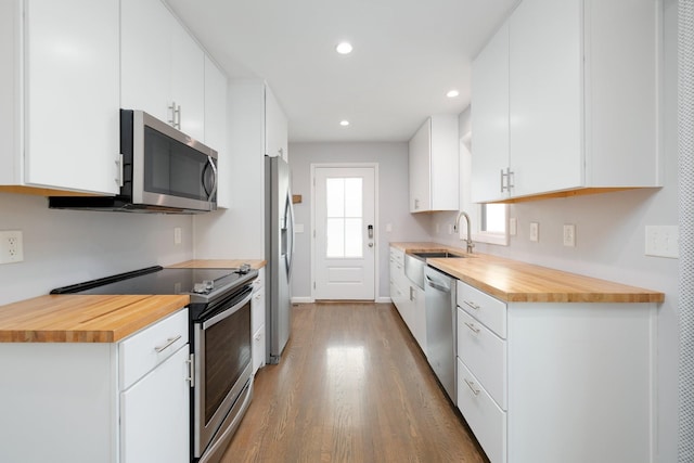 kitchen with stainless steel appliances, butcher block countertops, wood-type flooring, and white cabinets