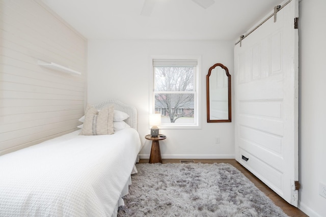 bedroom with dark wood-type flooring, ceiling fan, and a barn door