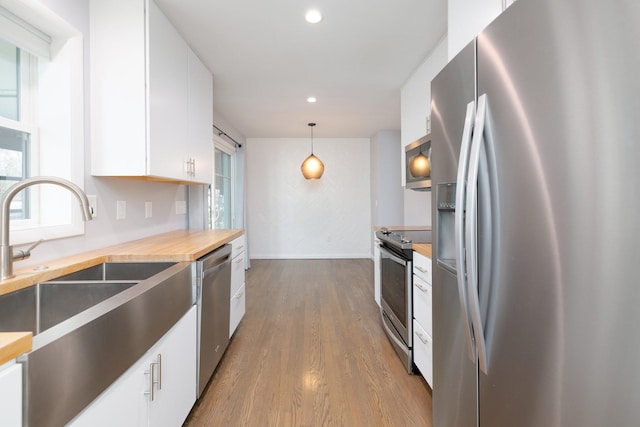 kitchen featuring appliances with stainless steel finishes, hardwood / wood-style floors, decorative light fixtures, sink, and white cabinets