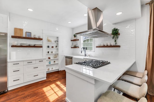 kitchen featuring island exhaust hood, appliances with stainless steel finishes, white cabinets, and a kitchen bar