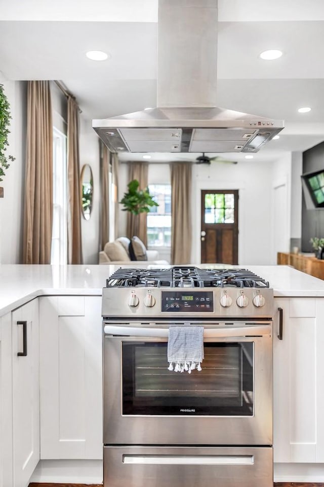 kitchen with island range hood, stainless steel range with gas stovetop, kitchen peninsula, and white cabinets