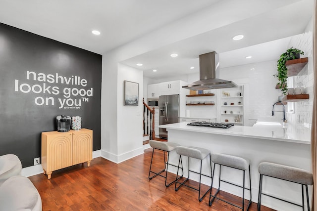 kitchen with sink, stainless steel appliances, island range hood, white cabinets, and kitchen peninsula