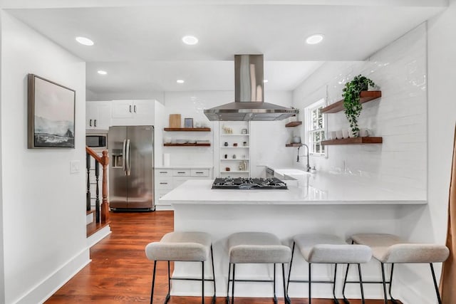 kitchen featuring a breakfast bar, island range hood, white cabinetry, kitchen peninsula, and stainless steel appliances