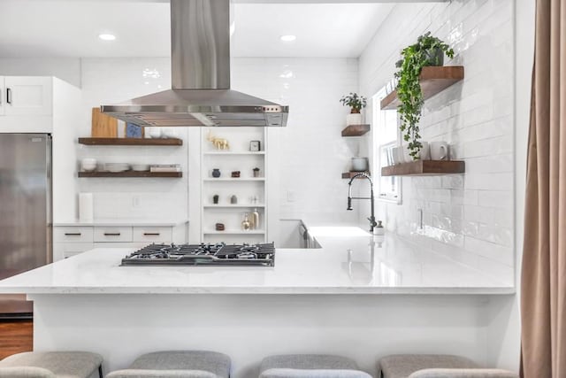 kitchen featuring white cabinetry, island range hood, a kitchen breakfast bar, and appliances with stainless steel finishes