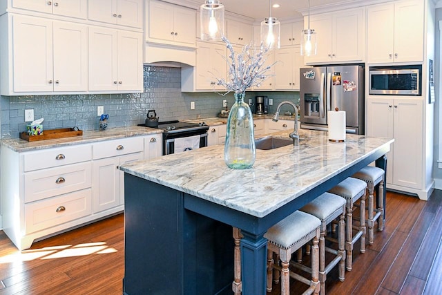 kitchen with appliances with stainless steel finishes, pendant lighting, a breakfast bar area, white cabinets, and a kitchen island with sink