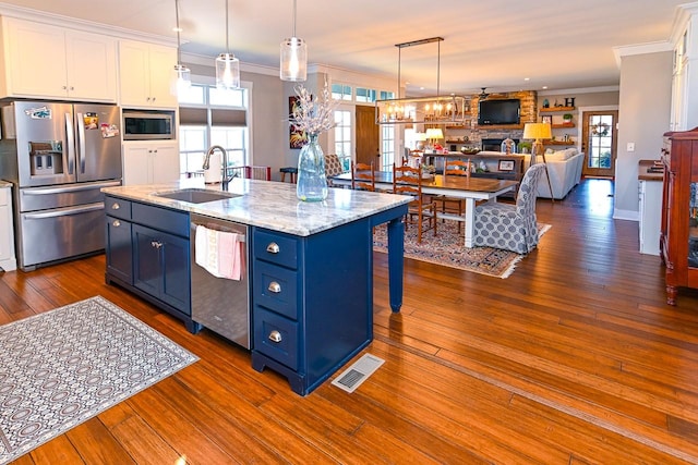 kitchen with pendant lighting, sink, stainless steel appliances, an island with sink, and white cabinets