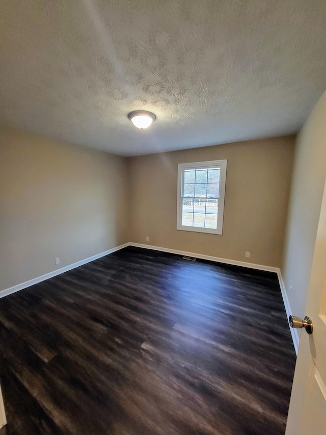 empty room with dark wood-type flooring and a textured ceiling