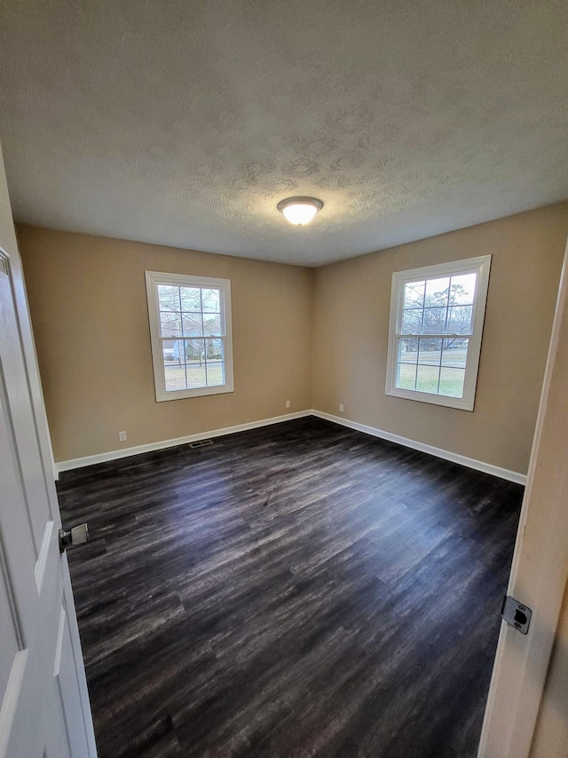 empty room featuring a healthy amount of sunlight, dark hardwood / wood-style floors, and a textured ceiling